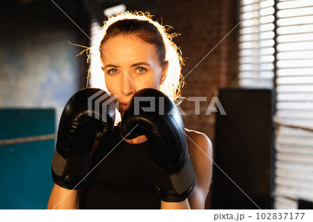Women self defense girl power. Strong woman fighter punching with boxing gloves to camera. Healthy strong girl punching training punches looking concentrated straight. Fit body workout Women self defense girl power. Strong woman fighter punching with boxing gloves to camera. Healthy strong girl punching training punches looking concentrated straight. Fit body workout 102837177