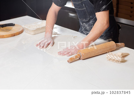 Dough for pizza, the chef rolls out the blanks. Closeup hand of chef baker in uniform white apron cook pizza at kitchen 102837845