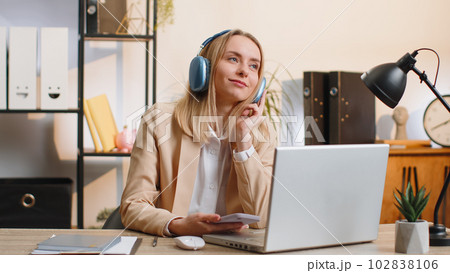 Young businesswoman working on laptop at home office wearing headphones listening favorite music 102838106