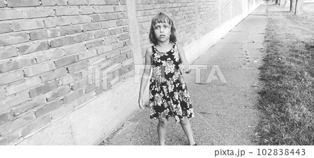 Girl scared. Halloween theme. A child in a dress with flowers against a brick wall is afraid. The girl sees a zombie on the street, is surprised and she is afraid. Black and white monochrome image 102838443