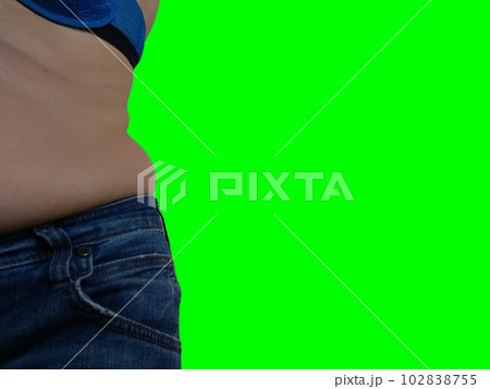 Saggy belly. Folds of leather and fat on the sides hanging over the waist of the jeans. Overeating or pregnancy. Obesity and Diabetes. Green chroma key background. Cellulite flabby muscles 102838755