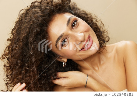 Woman applies cream and balm to her curly hair, the concept of protection and care, a healthy look, a smile with teeth on a beige background 102840283