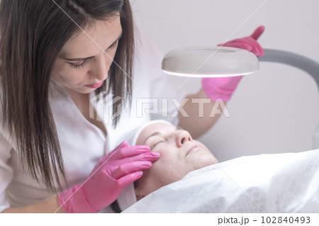 A skilled cosmetologist expertly performs facial procedures on a client at an aesthetic medicine clinic, including peeling and lifting massages in a relaxing spa or salon environment.  102840493