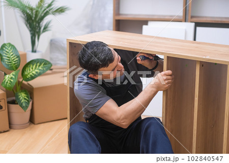 Custom furniture business skilled handyman assembling wooden rack tightening nails with professional instrument carpentry working process in customer house 102840547