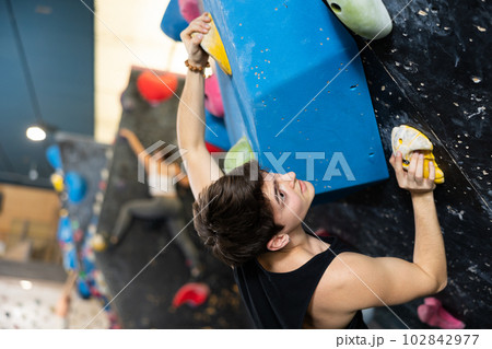 young muscular male sportsman climbing black wall for bouldering in gym 102842977