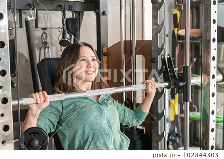 ジムでショルダープレスマシンを使って筋トレをする笑顔の日本人女性 ジムでショルダープレスマシンを使って筋トレをする笑顔の日本人女性 102844303