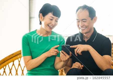 スマホを見ながら談笑するミドルの夫婦 102845557