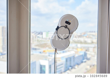 A window cleaner robot washes glass against the backdrop of multi-storey buildings. 102845689