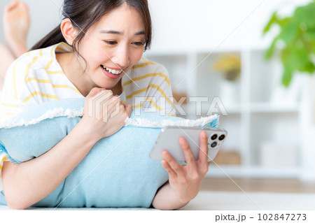部屋でスマホを操作する若い女性 102847273