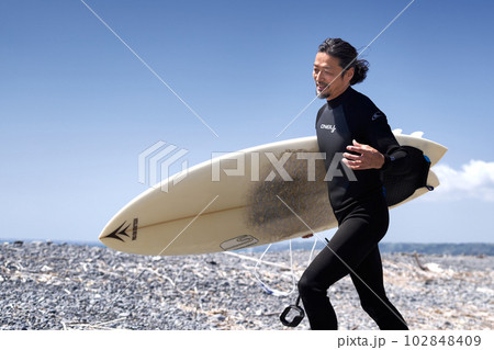 笑顔で海辺を歩くサーファーのミドル男性 102848409