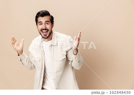 Portrait of a stylish man smile with teeth happiness opened his mouth in surprise on a beige background in a white t-shirt looks at the camera, fashionable clothing style, copy space, space for text 102848430