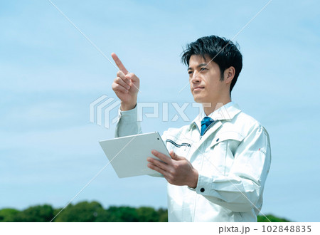 空を背景にタブレットを持つ作業服のビジネスマン 空を背景にタブレットを持つ作業服のビジネスマン 102848835