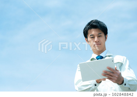 空を背景にタブレットを持つ作業服のビジネスマン 102848842