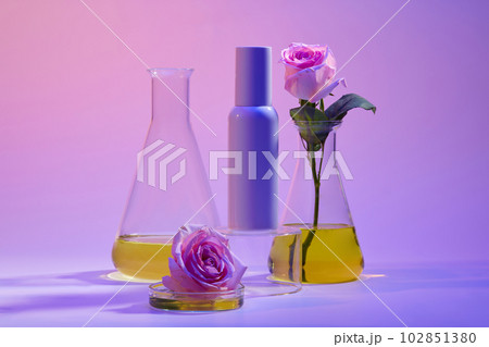 Unlabeled cosmetic container placed on a podium, glass petri dish and erlenmeyer flask of yellow fluid displayed around. Natural beauty product concept 102851380