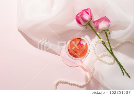 Cocktail glass filled with liquid extracted from Rose (Rosa) and a pearl necklace displayed on chiffon fabric. Blank space can be used to promote natural cosmetic product 102851387