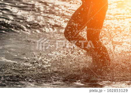 Running woman on a summer beach. A woman jogging on the beach at sunrise, with the soft light of the morning sun illuminating the sand and sea, evoking a sense of renewal, energy and health. Running woman on a summer beach. A woman jogging on the beach at sunrise, with the soft light of the morning sun illuminating the sand and sea, evoking a sense of renewal, energy and health. 102853129