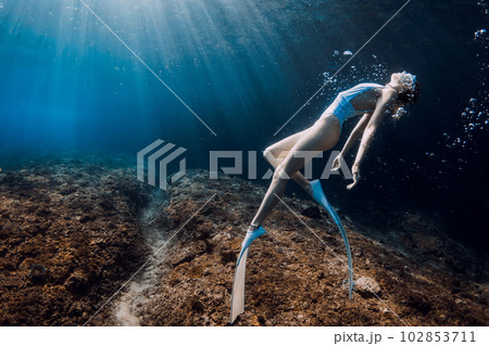 Woman freediver relaxing underwater in blue sea. Freediving with beautiful girl in transparent ocean and sun rays Woman freediver relaxing underwater in blue sea. Freediving with beautiful girl in transparent ocean and sun rays 102853711
