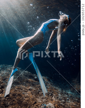 Woman freediver glides underwater in blue sea. Freediving with girl in deep ocean and sun rays Woman freediver glides underwater in blue sea. Freediving with girl in deep ocean and sun rays 102853712