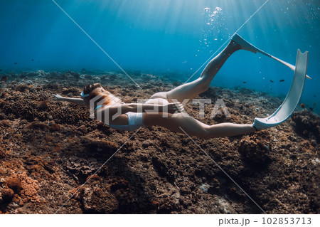 Woman freediver glide with fins underwater over corals. Freediving in tropical blue ocean 102853713