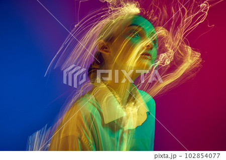 Portrait of young girl posing over gradient blue pink studio background with neon lights effect. Creative vision 102854077