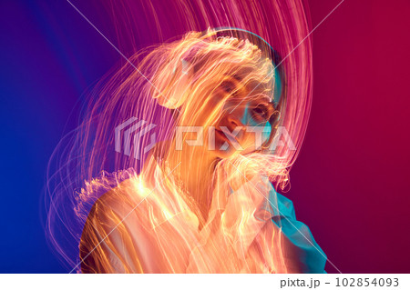 Portrait of young girl listening to music in headphones, posing over gradient background with mixed neon lights effect 102854093