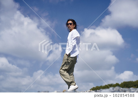 青空のもとポケットに手を入れて歩くミドルシニア男性　ポートレート 102854588