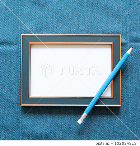 Navy picture frame with white blank paper and pencil on blue fabric background. top view, copy space 102854815