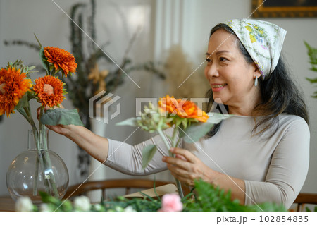 Beautiful senior woman arranging flowers in vase at her floral shop. Floristry, small business and people concept 102854835