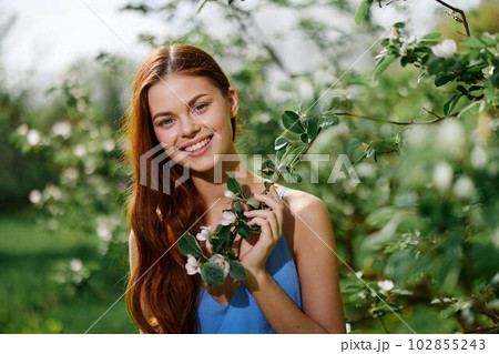 Woman portrait beautifully smiling with teeth spring happiness in nature against a green tree tenderness hand touching a branch of a blooming tree, safety from allergies and insects 102855243
