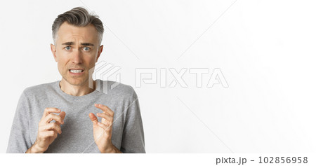 Close-up of anxious middle-aged man, looking scared and nervous, feeling guilty, standing over white background 102856958
