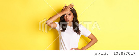 Portrait of annoyed african-american girl, slap forehead and roll her eyes bothered, forgot something important, standing over yellow background Portrait of annoyed african-american girl, slap forehead and roll her eyes bothered, forgot something important, standing over yellow background 102857017