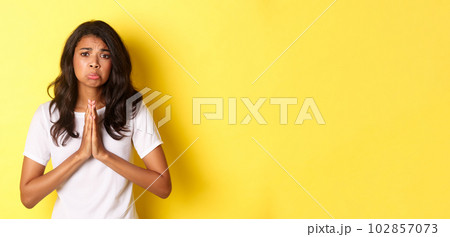 Portrait of sad african-american girl pleading, begging for help and sulking upset, standing over yellow background 102857073