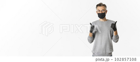 Covid-19, pandemic and social distancing concept. Image of middle-aged man in black medical mask, gloves and glasses showing thumbs-up, protect himself from catching coronavirus 102857108