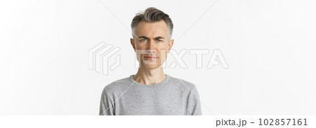 Close-up of skeptical middle-aged man, frowning and looking doubtful at camera, standing over white background in gray sweater Close-up of skeptical middle-aged man, frowning and looking doubtful at camera, standing over white background in gray sweater 102857161