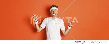 Concept of sport, fitness and lifestyle. Cheerful middle-aged sportsman with headband, smiling happy and pointing fingers sideways, showing left and right copy space Concept of sport, fitness and lifestyle. Cheerful middle-aged sportsman with headband, smiling happy and pointing fingers sideways, showing left and right copy space 102857209