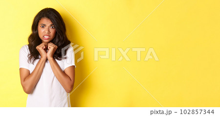 Portrait of cute african-american girl looking scared and reluctant, grimacing displeased, standing over yellow background 102857344