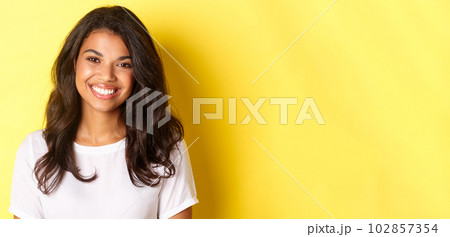 Close-up of attractive african-american woman, smiling and looking happy, standing over yellow background 102857354
