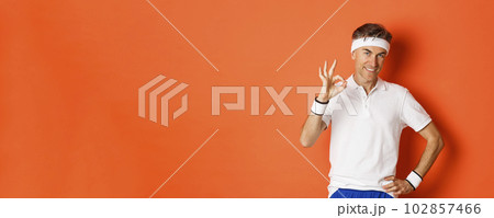 Concept of sport, fitness and lifestyle. Portrait of confident middle-aged sportsman, showing okay sign and look pleased, guarantee something or recommending gym, orange background 102857466