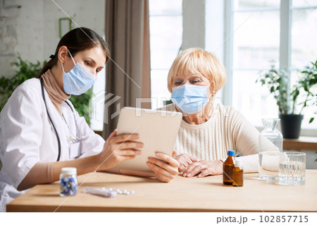 Female doctor and senior woman, patient wearing face mask, having appointment in office. Checkup and treatment after virus 102857715