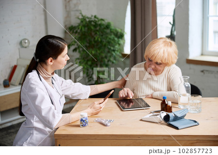 Senior woman and female doctor using gadgets to check patient's health information. In office. Modern medical attitude Senior woman and female doctor using gadgets to check patient's health information. In office. Modern medical attitude 102857723
