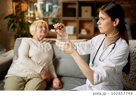 Female doctor dropping meds, drops for her senior female patient sitting on couch. Taking care after health with medicine 102857749