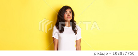 Portrait of hopeful young african-american girl, longing for something, looking at upper left corner dreamy, standing over yellow background 102857750