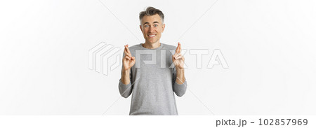 Image of excited and hopeful middle-aged man making a wish, waiting for results, cross fingers for good luck and smiling, standing over white background Image of excited and hopeful middle-aged man making a wish, waiting for results, cross fingers for good luck and smiling, standing over white background 102857969
