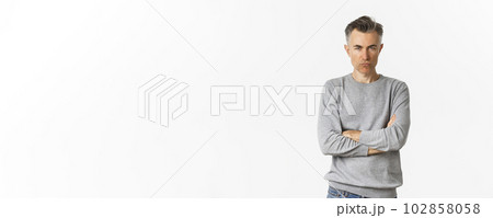 Image of angry middle-aged man feeling offended, cross arms on chest and squinting at camera, standing over white background 102858058