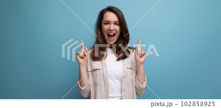 ecstatic 30s dark haired woman in beige shirt on blue background 102858925