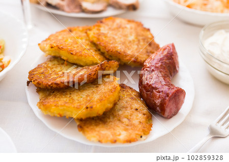 Fried grated potato pancakes with fried sausage on white plate Fried grated potato pancakes with fried sausage on white plate 102859328