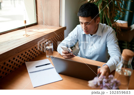 Portrait with handsome man, freelancer wearing shirt sitting at cafe and working online on laptop. Distance job 102859683