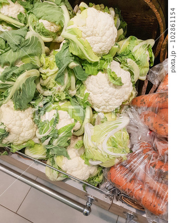 Close-up of cauliflower and fresh raw carrots in plastic bags on the counter in the store. Retail sale of vegetables Close-up of cauliflower and fresh raw carrots in plastic bags on the counter in the store. Retail sale of vegetables 102861154