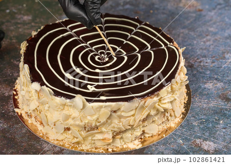 Esterhazy cake. Pastry chef decorates chocolate glaze with wooden stick 102861421