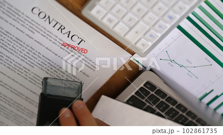 Manager hand putting red stamp approved on contract document closeup 102861735
